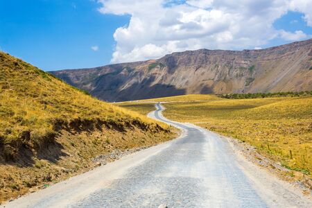 The road among the mountains. Cobbled road in the crater of Nemrut volcano, Bitlis Province, Eastern Turkey. Panoramic view of golden fields, hills and mountainsの写真素材