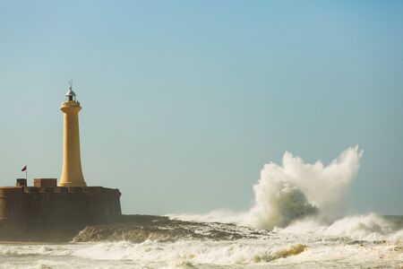 Lighthouse on the rocks. Stormy weather at sea. Big waves on the promenade in Rabat, the capital of Morocco. Waves breaking on the rocks. Crashing waves at the lighthouse in sunny weatherの写真素材