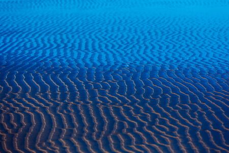 Abstract blue background. Sand ripples and waves. Sunny ocean view. Wavy texture of water surface. Relaxing seascapeの写真素材