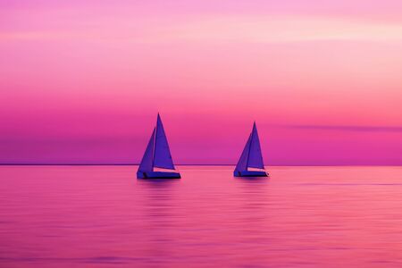 Sailing boat yachts in the sunlight. Sailboats at the sunset. Luxury vacation. Summer adventures. Blurred sea water. Maritime competitions. Regatta raceの写真素材
