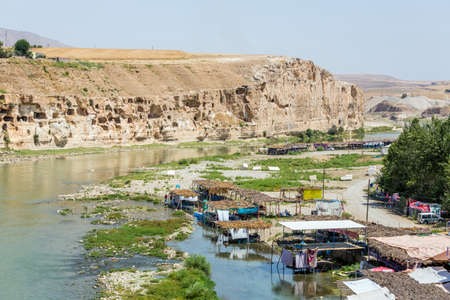 Hasankeyf, Turkey, 08.23.2014: The view of the Tigris River valley, cliffs with stone caves. Various cafes right in the river water under awningsのeditorial素材