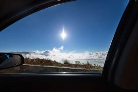 View from the car window to the mountains, blue sky and the sun. Car in the clouds. Traveling by...