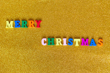 Merry Christmas text on a golden background. Colorful wooden letters on a shiny glitter surface....