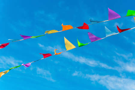 Colorful bunting flags in the wind. Festive background for holidays, anniversary, celebration. Multi-colored flag garland against a blue saturated skyの写真素材