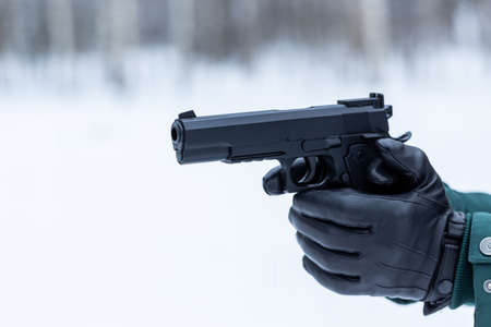 Gun in hand close-up. Black leather gloves with a pistol. Shooting in nature.の写真素材