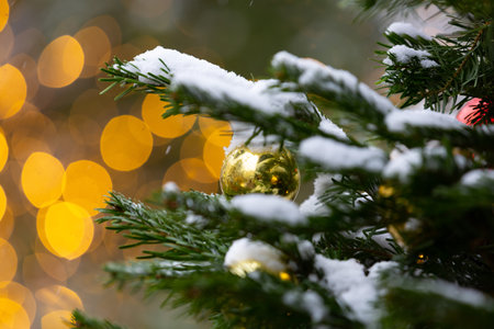Christmas ball on a fir branch in the snow. Beautiful bokeh. Blurred background with Christmas lights. Winter festive background with hanging balls and yellow lightsの写真素材