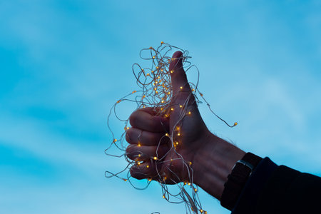 Thumb up in Christmas lights. Man showing thumbs on the blue background. New Year and Christmas...