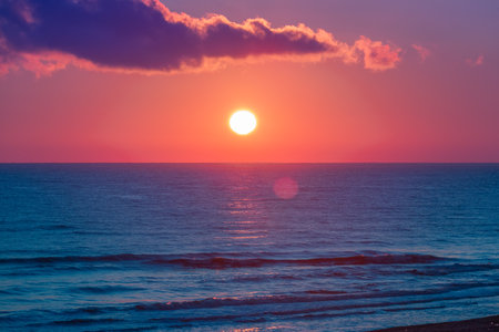 Stunning sunrise at Caspian Sea in Derbent, Dagestan. Sun disc over the horizon. Bright backlit sky and clouds. Silhouettes of waves in the rays of the sun. Incredible wallpaperの写真素材
