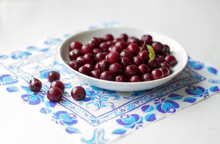 Burgundy cherries in the white saucer on the window-sill. White saucer with cherries on the napkin.の写真素材