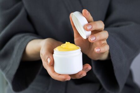 Woman holding opened plastic container with yellow cream in her hands.