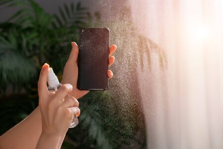 Women hands is spraying disinfectant spray on smartphone. Beautiful photo with sunlight.の写真素材