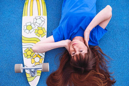 Portrait of young women with skateboard on blue background. Woman wears blue T-shirt.の写真素材