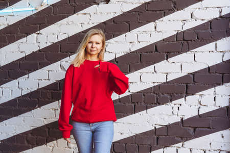 Woman in a red sweatshirt stands against a black and white roller wall.の写真素材