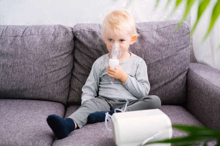Cute little blond boy does inhalation at home.の写真素材