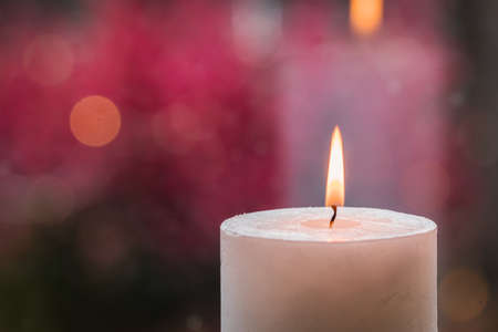 Close up photo of white burning candle on pink background.の写真素材