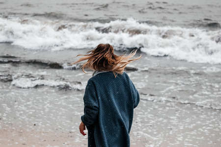 Woman walking on the snowy beach during a thunderstorm.の写真素材