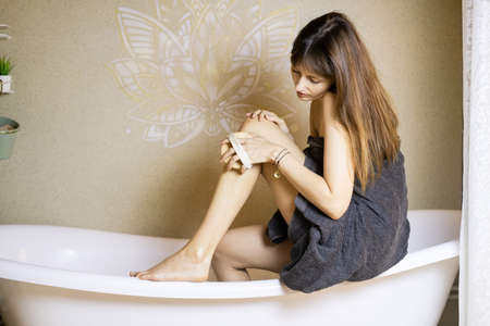 Naked brunette woman relaxing in bathtub and using dry brush massager.