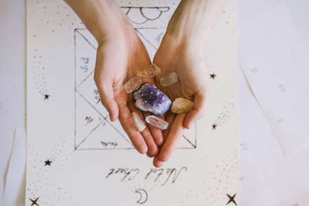 Woman holding crystals in her hands. Natal chart and background.