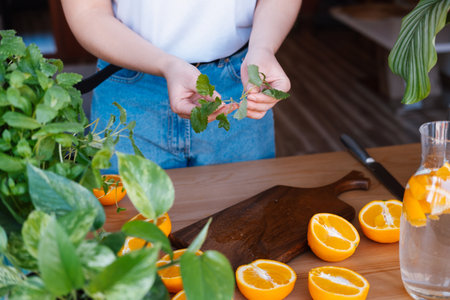 Woman prepare orange infused water with peppermint, summer drink.の写真素材