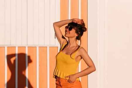 Young woman in tank top and orange standing still near orange beach house.の写真素材