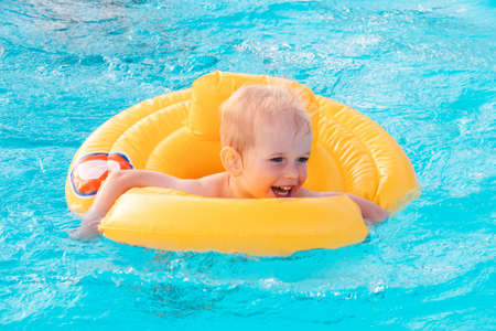 Toddler boy swimming with inflatable floatie in swimming pool on a sunny day.