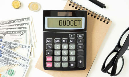 Budget 2020 text concept. Office workplace table with calculator, glasses, textbook and keyboardの写真素材