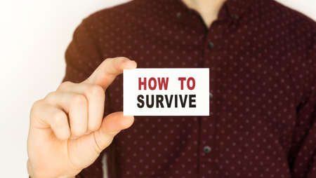Businessman holding a card with text HOW TO SURVIVE.の写真素材