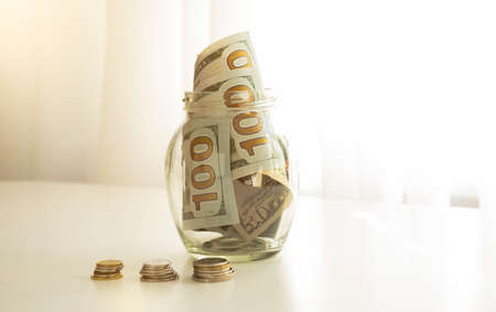 Many 100 US dollars bank notes in a glass jar isolated on white backgroundの写真素材