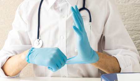 A Doctor Wearing A Protective Apron And Protective Helmet Puts On Rubber Gloves During An Ongoingの写真素材