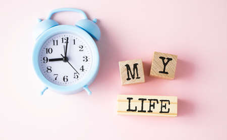The text is my life on wooden blocks on a bed-pink background and a blue alarm clock.の写真素材