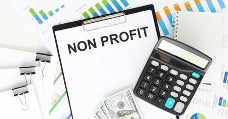 NON PROFIT. TEXT ON WHITE PAPER ON BLACK ENVELOPE OVER THE FINANCIAL GRAPHICS AND THE CALCULATOR VIEW FROM ABOVE. CLOSE-UP. CAPITAL LETTERS BUSINESS CONCEPTの写真素材