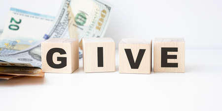 Glass jar with coins and the word give on wood block. Saving Money for giving and donation concept.の写真素材