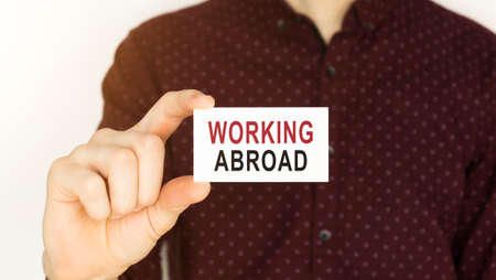 Businessman holding a card with text WORKING ABROAD.の写真素材