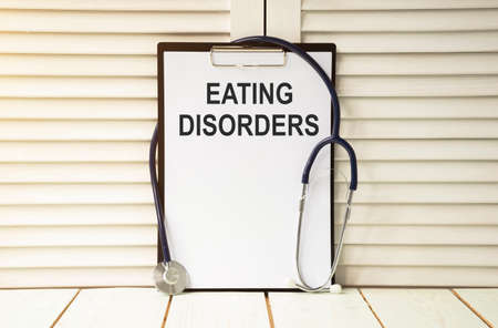 An eating disorder is written on a white sheet, which stands on a wooden table and a stethoscope. Medical conceptの写真素材