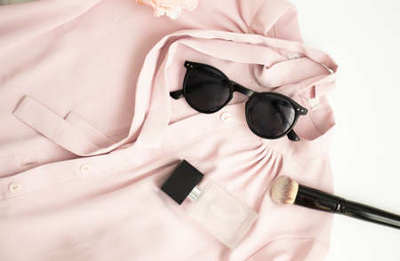 Flatlay women pink shirt, sunglasses, jar with perfume, accessories on pink fur
