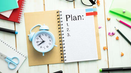 Notepad with the text: Plan, on a wooden table with an alarm clock and office items. Planning concept.の写真素材