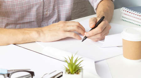 Close up of woman's hands writing in spiral notepad placed on wooden desktop with various itemsの写真素材