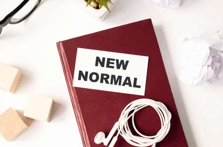 NEW NORMAL text with notebook, safety face mask, keyboard, fountain pen, hand sanitizer and decorative plant on wooden background. Covid 19 and coronavirus conceptの写真素材