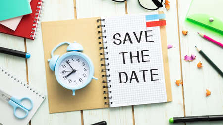 White sheet of notepad paper with the text Save The Date on a wooden background.の写真素材
