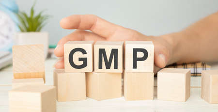 Good Manufacturing Practice. GMP the word on wooden cubes, cubes stand on a reflective surface, in the background is a business diagram. Business and finance conceptの写真素材