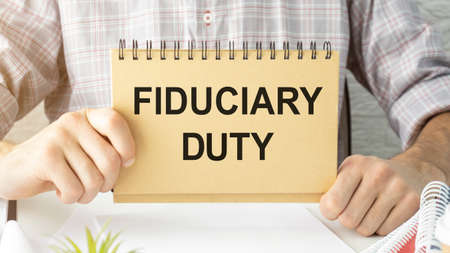 Text FIDUCIARY DUTY is written on a notebook with a pen and a magnifying glass lying on the table. Business concept.の写真素材