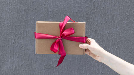 Valentine gift. Beauty Woman hands holding Gift box with red bow over holiday background with glowing hearts bokeh, close-up. pastel colors. Wide angle format backdropの写真素材