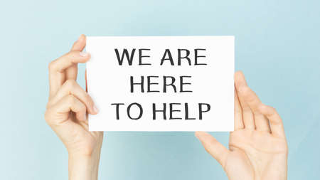 WE ARE HERE TO HELP written on a white sheet held by a person. Sponsorship conceptの写真素材