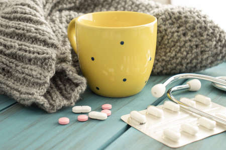 Cold tea, pills, knitted scarf and stethoscope. Cold season.
