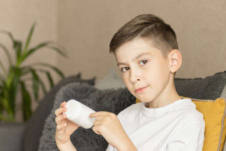 Sick Boy sits on the couch and looks at a jar with pills in his hands. Cold and flu season.の写真素材