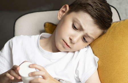 Sick Boy sits on the couch and looks at a jar with pills in his hands. Cold and flu season.