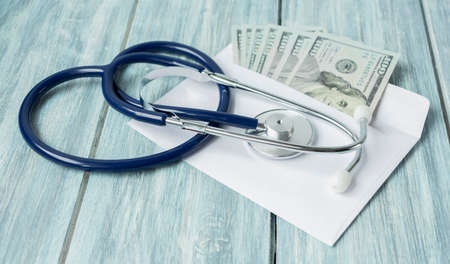 Envelope with money and a stethoscope on wooden background