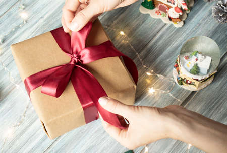 Christmas gift. Congratulations.Top wiew of woman holding traditional decorated gift box. Wooden table with cane, fir branches, fir cone, and berriesの写真素材