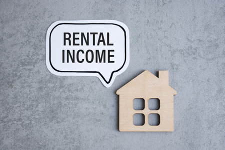 Handwriting: rental income and wooden house figurine.の写真素材