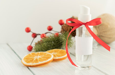 Bottle of hand gel sanitizer with Christmas decoration and ribbon as a gift. Concept of spending Christmas during coronavirus pandemic lock down and quarantine. Red glittery background.の写真素材
